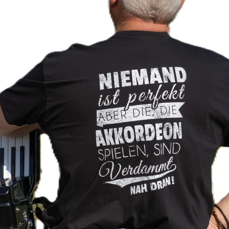 Arie von hinten mit T-Shirt-Spruch: „Niemand ist perfekt, aber Akkordeonspieler sind verdammt nah dran“